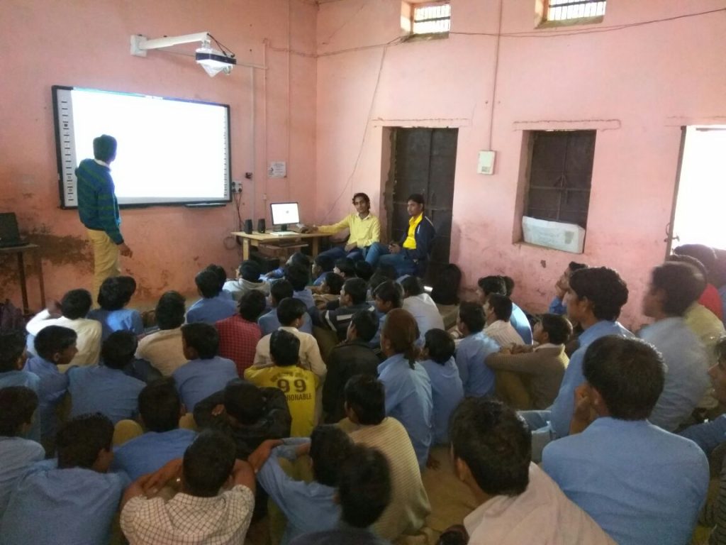 Students attend an SGJSS smart-class session with a projector screen in a rural Rajasthan school.